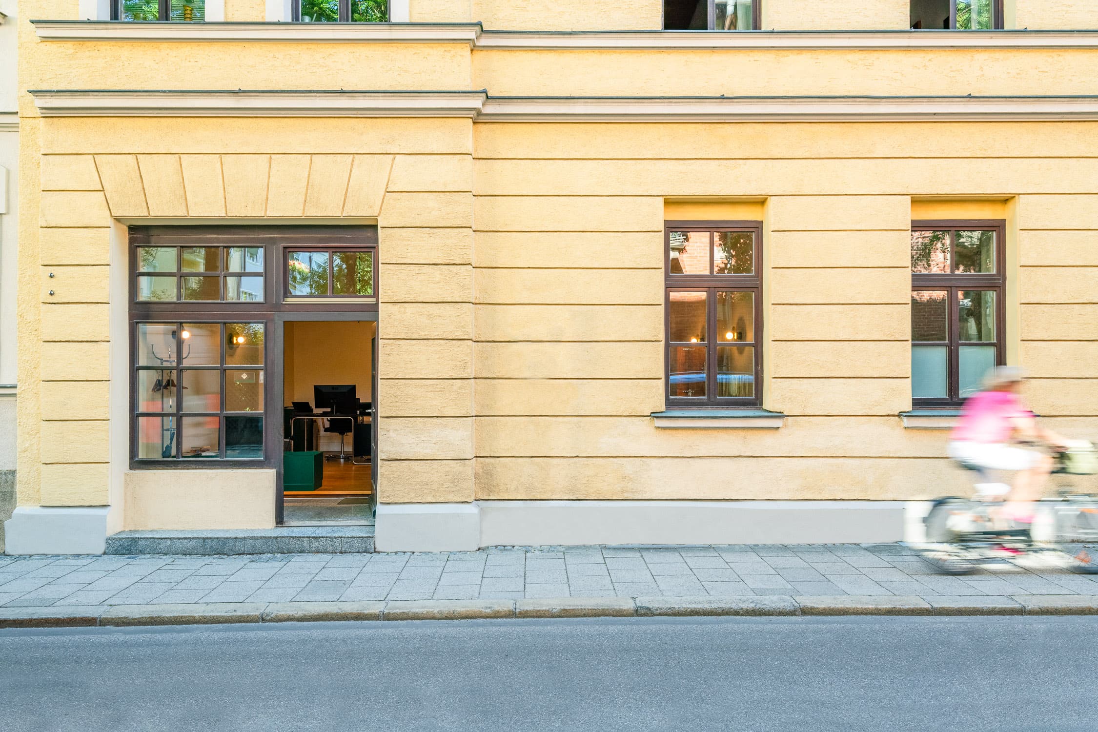 Bürofassade Mandlstraße 22 mit offener Tür und vorbeifahrender Radfahrerin, München-Schwabing