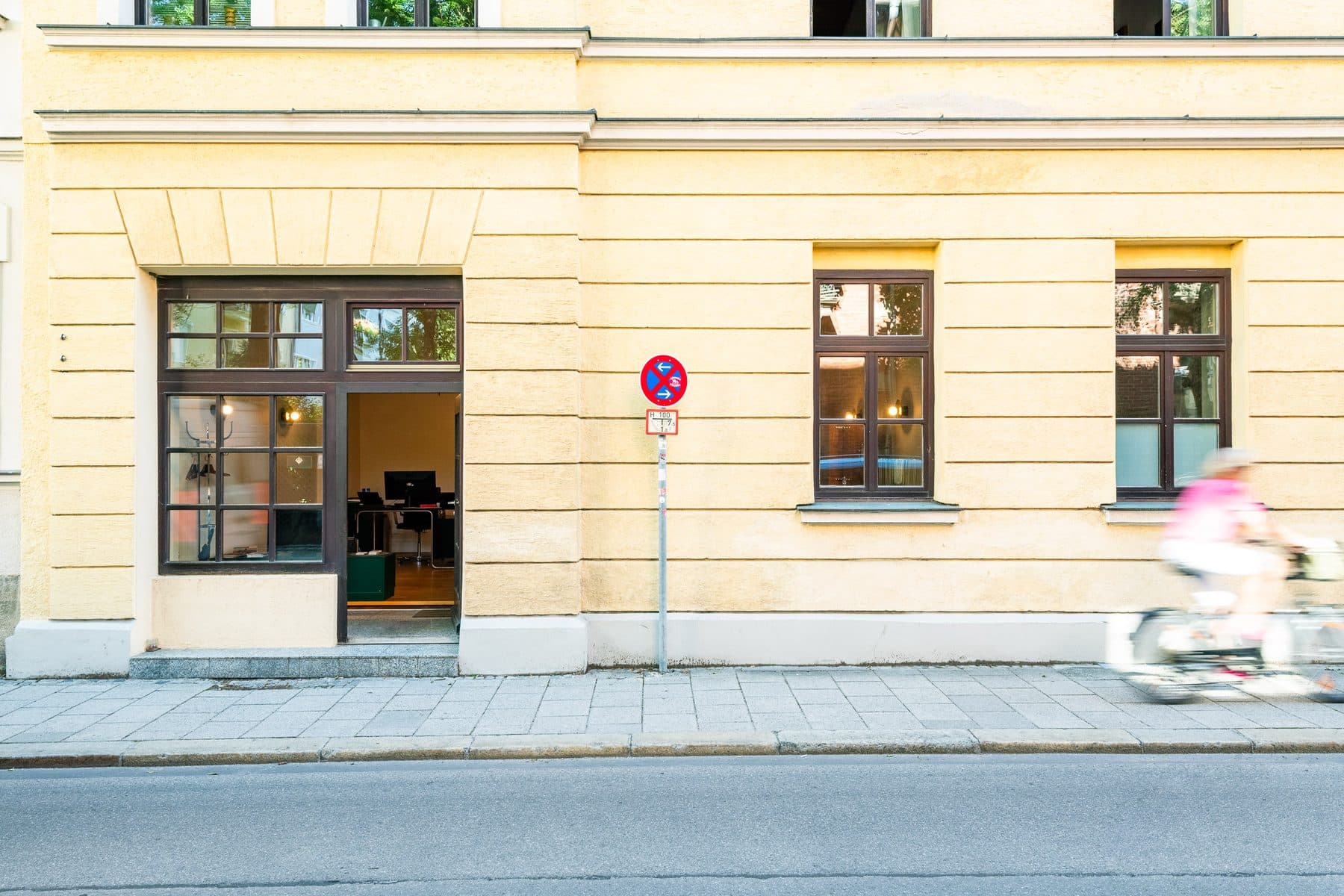 Bürofassade Mandlstraße 22 mit offener Tür und vorbeifahrender Radfahrerin, München-Schwabing