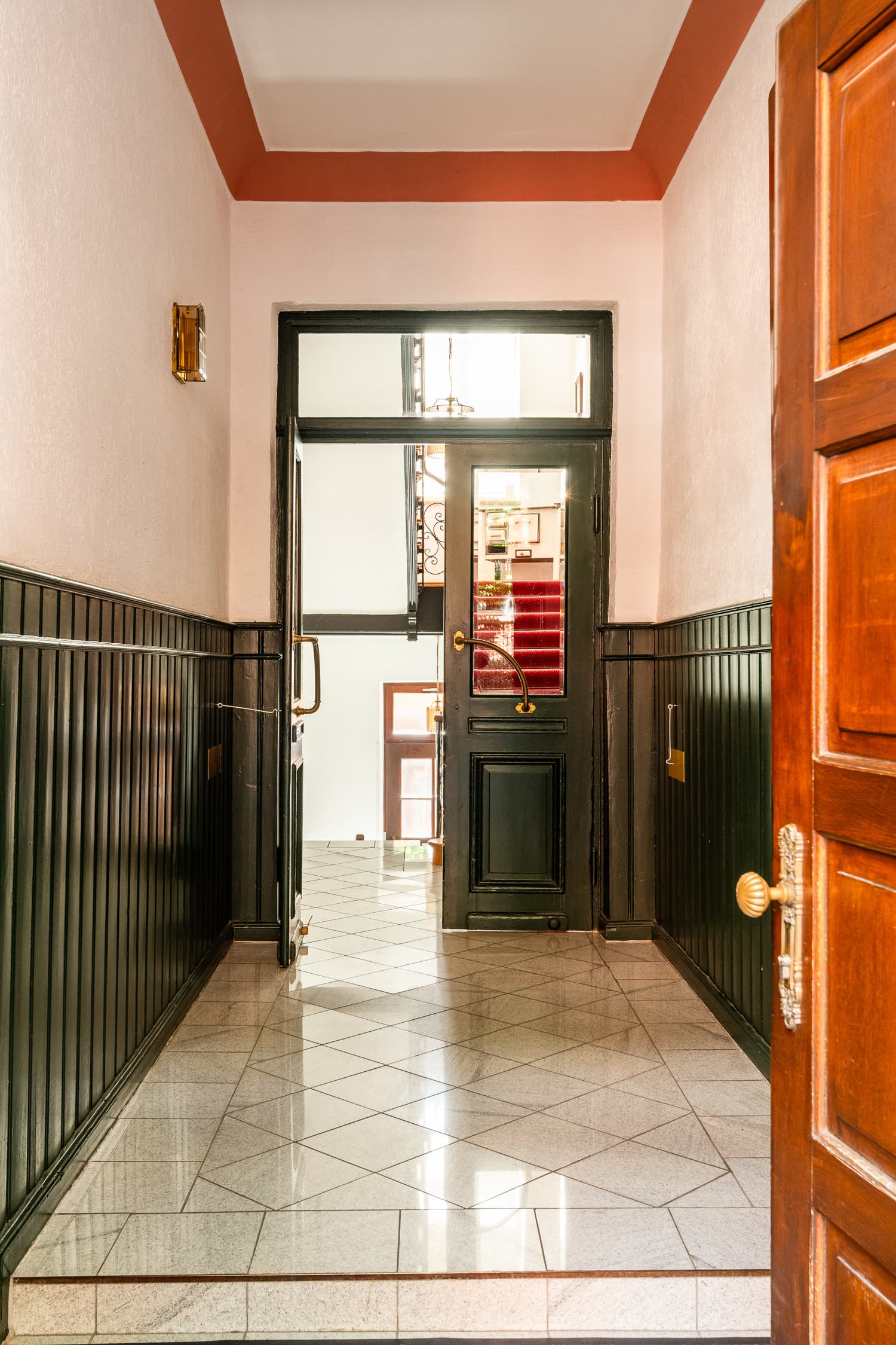 Altbau-Treppenhaus mit dunkelgrüner Täfelung und rotem Läufer
